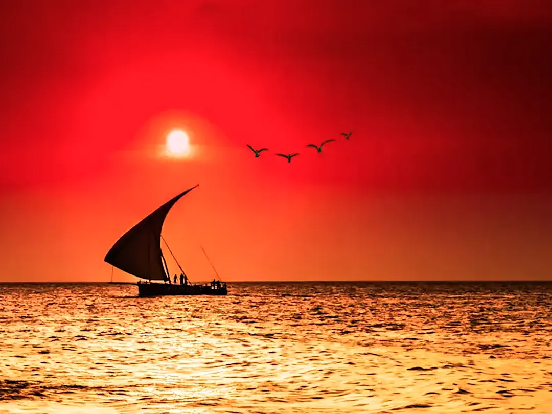 Traditionelles Dhow-Boot bei Sonnenuntergang mit rotem Himmel, Sansibar, Tansania.