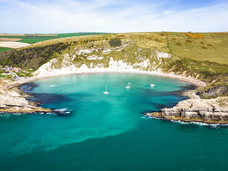 Lulworth Cove, Dorset, Großbritannien Die malerische Lulworth Cove in Dorset, Großbritannien, mit ihrem einzigartigen halbmondförmigen Strand und beeindruckenden Klippen, die durch natürliche Erosion entstanden sind