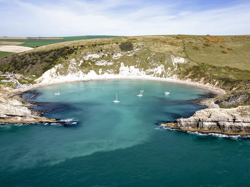 Lulworth Cove, Dorset, Großbritannien Die malerische Lulworth Cove in Dorset, Großbritannien, mit ihrem einzigartigen halbmondförmigen Strand und beeindruckenden Klippen, die durch natürliche Erosion entstanden sind