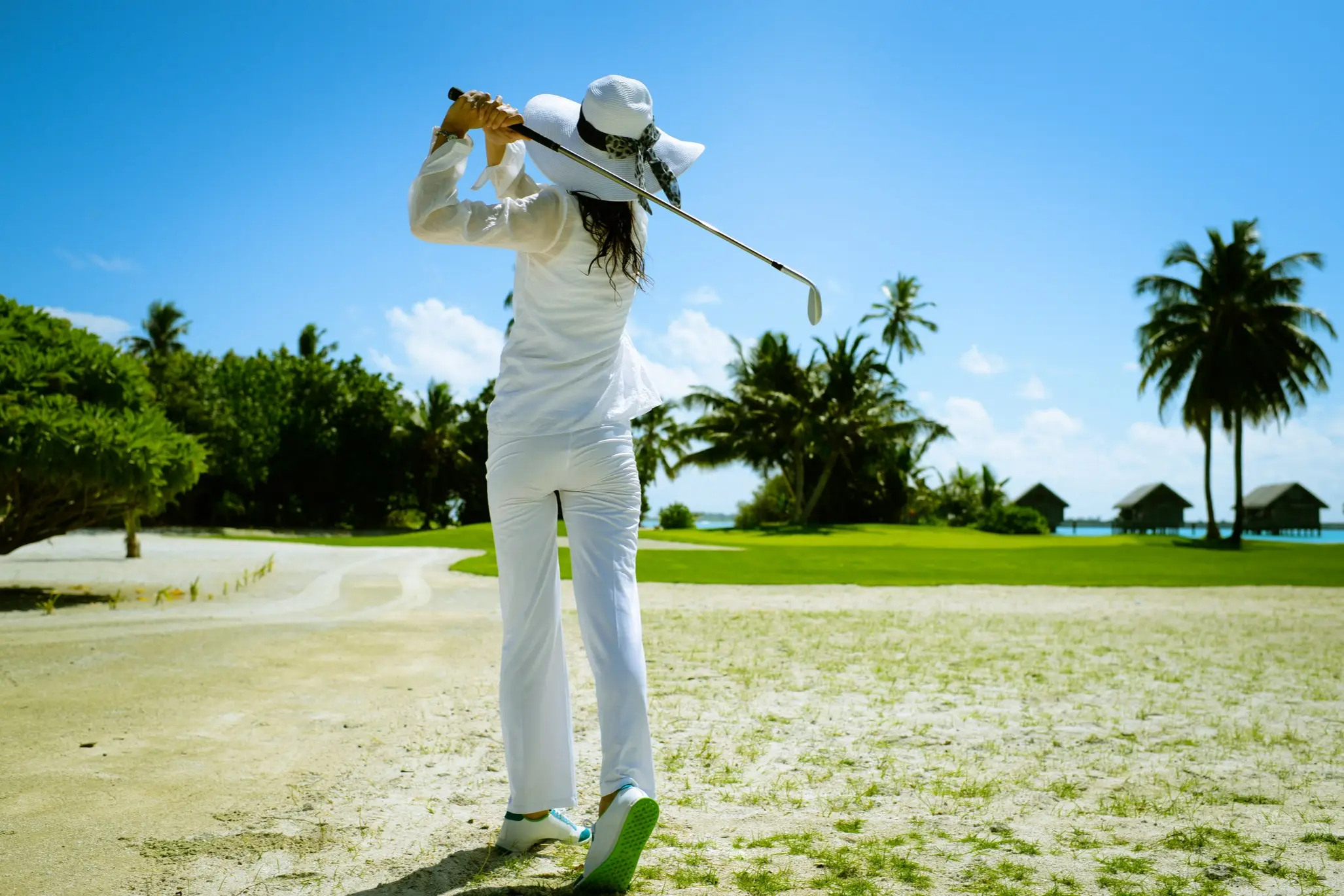 Mauritius, Golferin Frau spielt in heller, langer Kleidung Gold und trägt dabei einen Sonnenhut