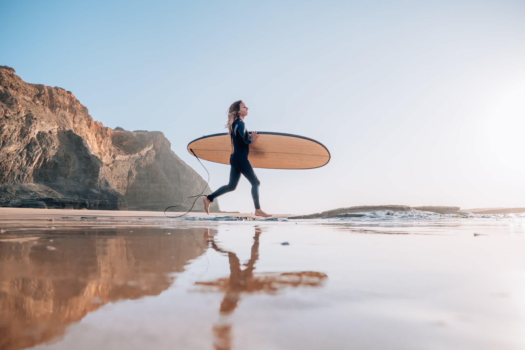Femme surfeuse courant sur la plage au lever du soleil, Portugal