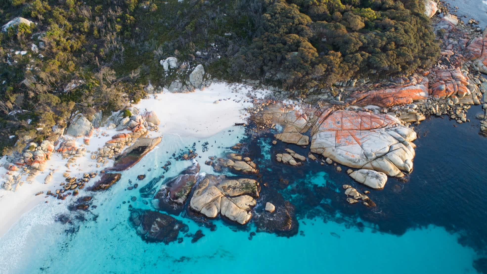Australie, Tasmanie, une mer d'un bleu azur et des rochers aux reflets rouges sur la côte est.