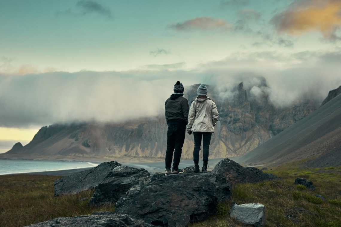 Ein Paar Wanderer an einem isländischen Strand mit einer Bergkette im Hintergrund.