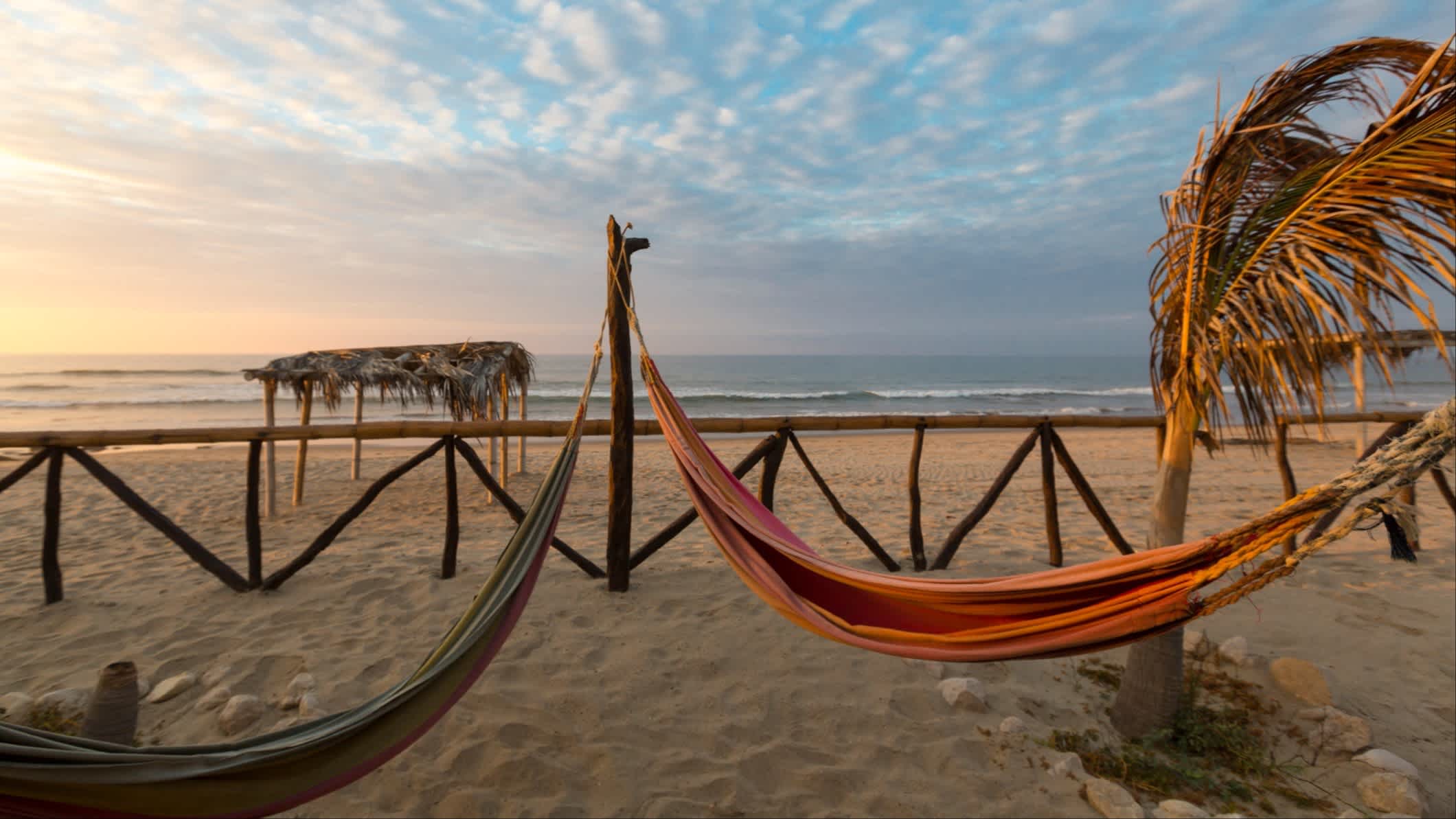 Der Strand Punta Sal in Mancora, Peru mit Hängematten, einer Palme und einer kleinen Strohhütte im Bild bei Sonnendämmerung.