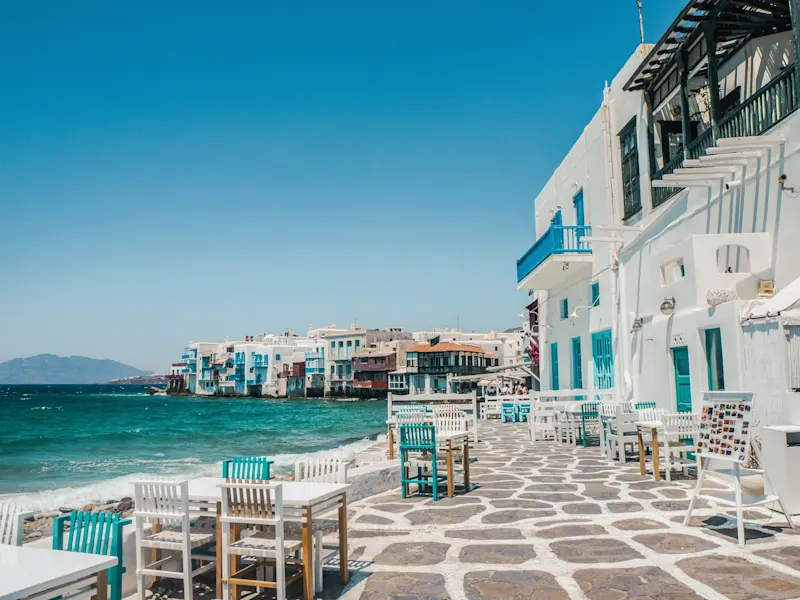 Woman in a blue dress walks through a narrow, white alley with blue details. Mykonos, Cyclades, Greece.