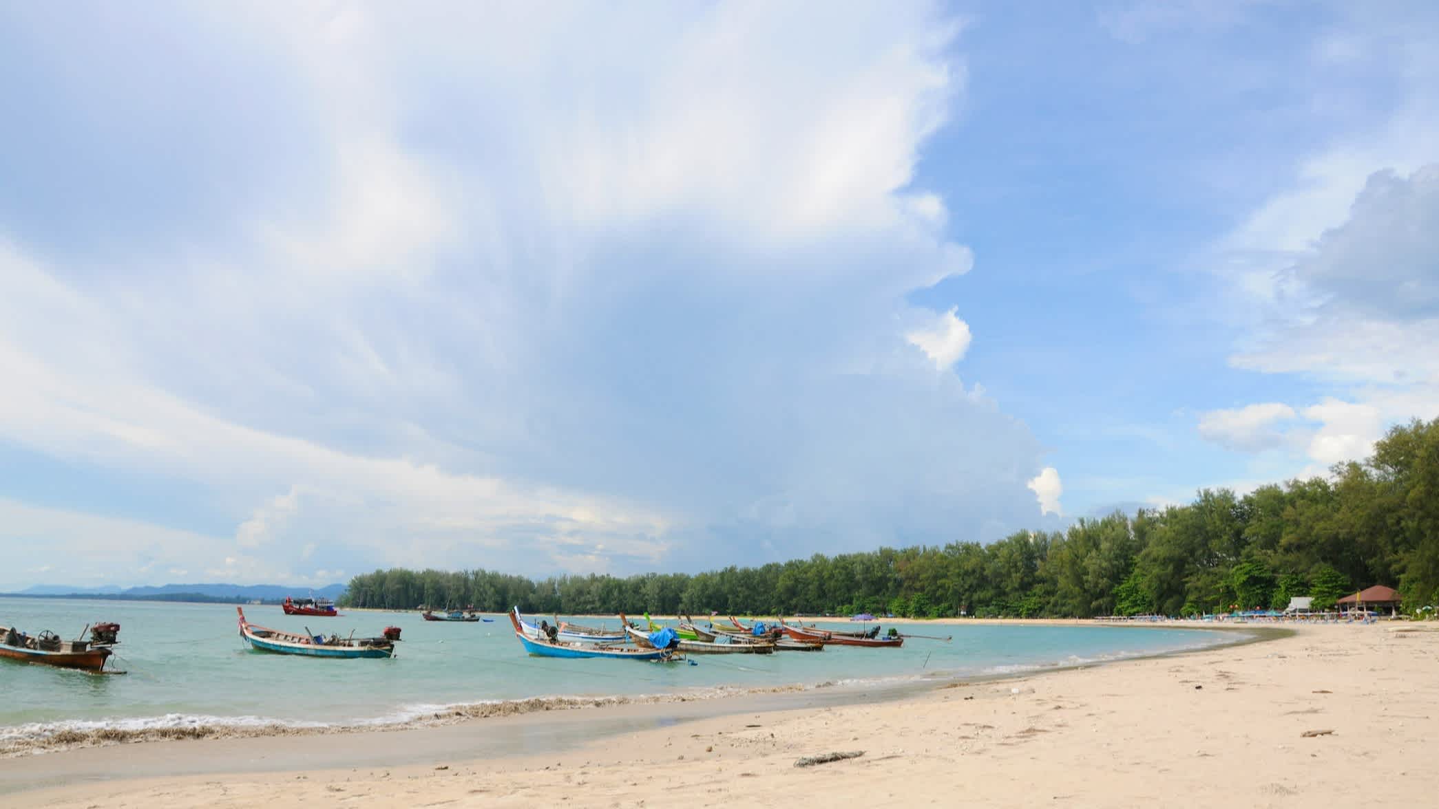 Der Nai Yang Beach auf Phuket mit Booten auf dem Wasser und Wolken am Himmel.