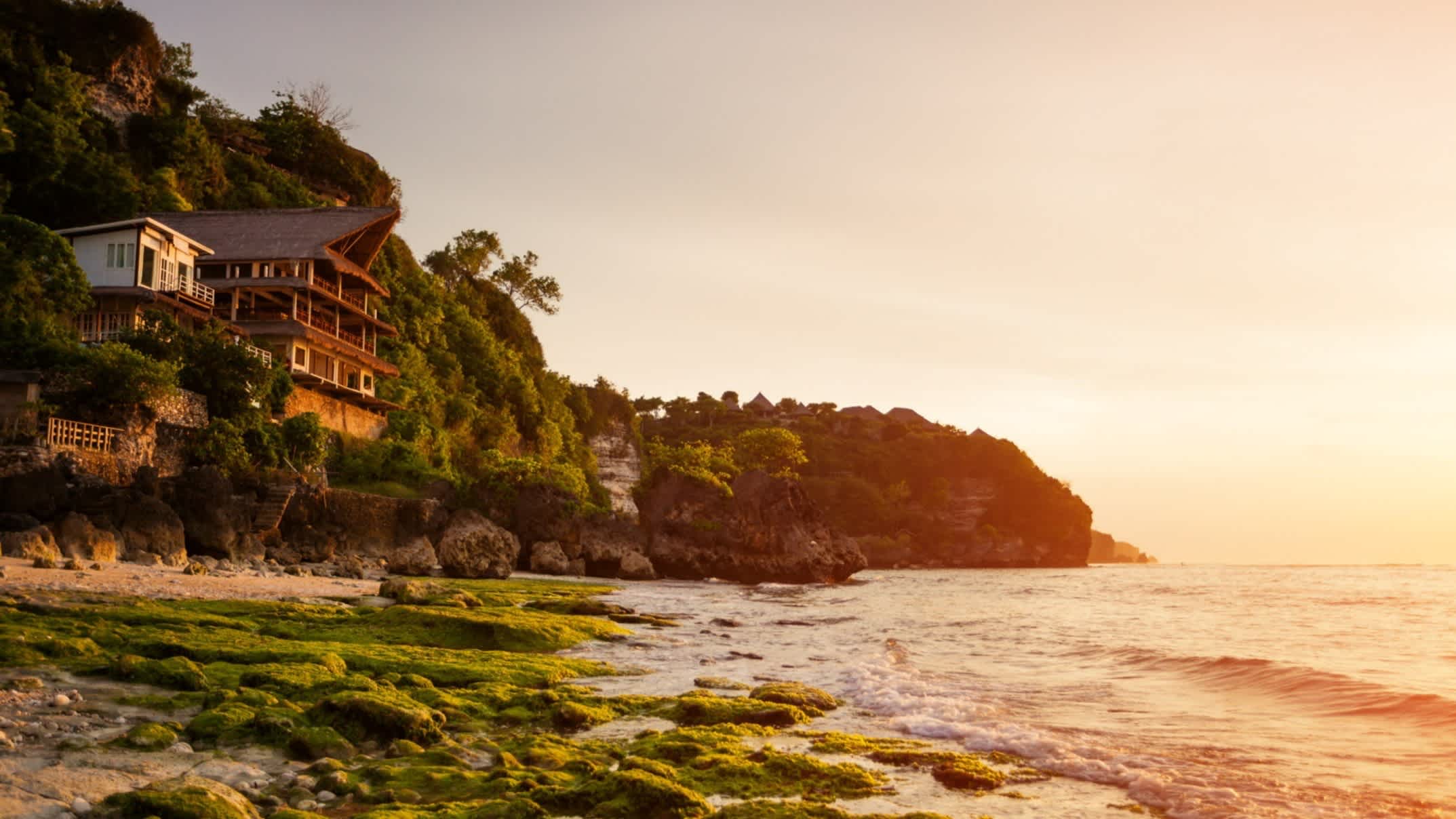 Ein Haus an der Klippe des Bingin Beach, Indonesien mit Blick auf das Wasser sowie bei Sonnenuntergang.