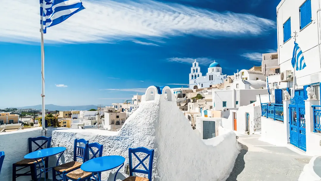 Weiße Häuser mit blauen Dächern und griechischer Flagge. Pyrgos, Santorini, Griechenland.