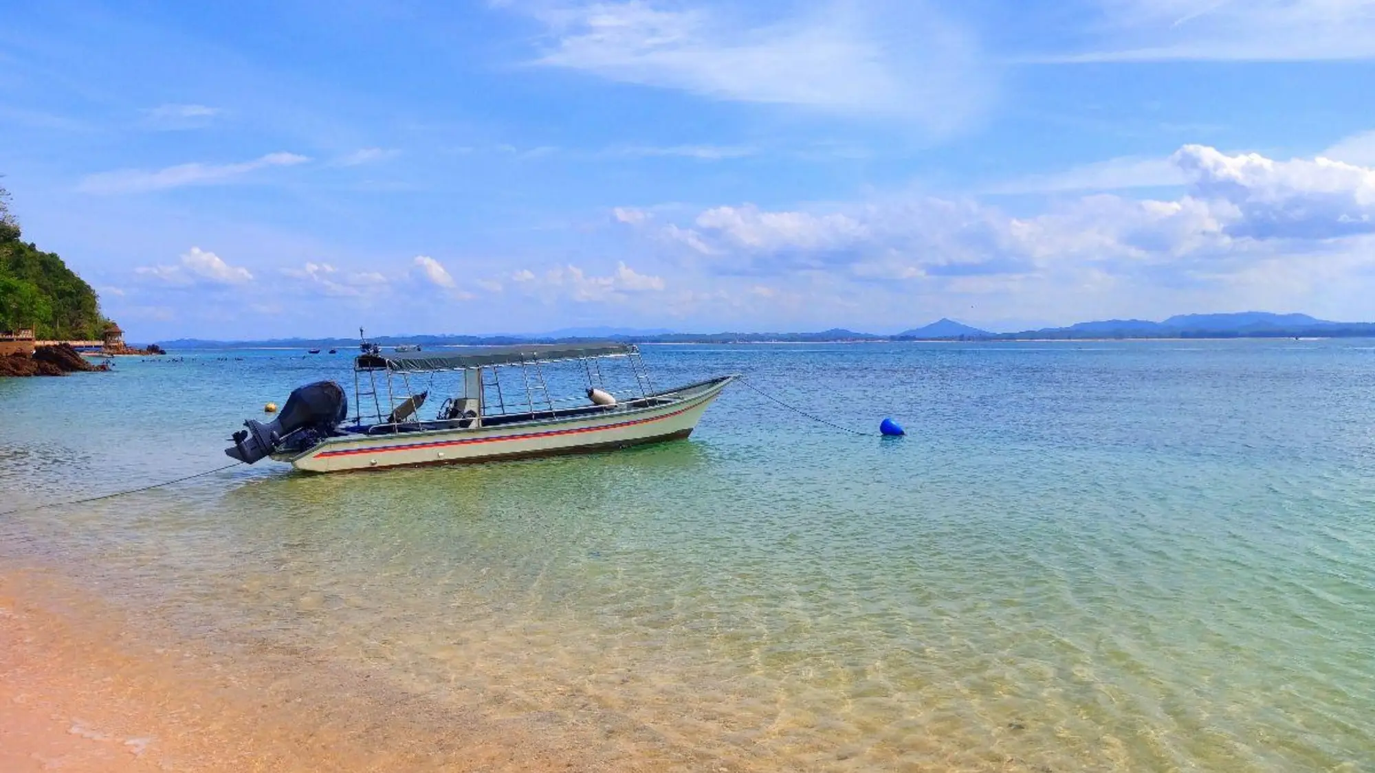 Boot auf klarem Wasser vor einer tropischen Küste unter blauem Himmel, Pulau Kapas, Malaysia.