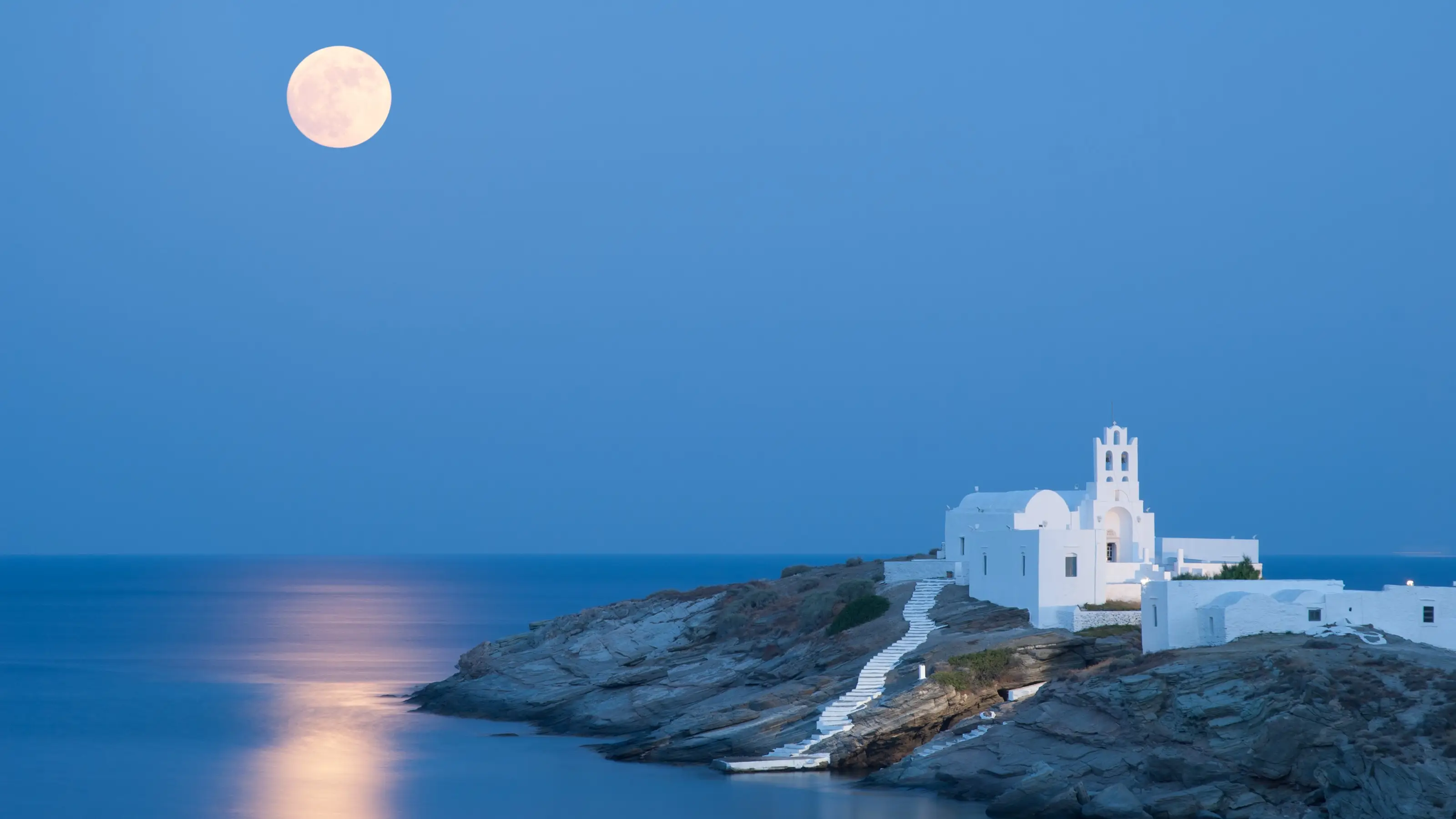 Une chapelle blanche sur une côte rocheuse éclairée par la pleine lune, Sifnos, Cyclades, Grèce.