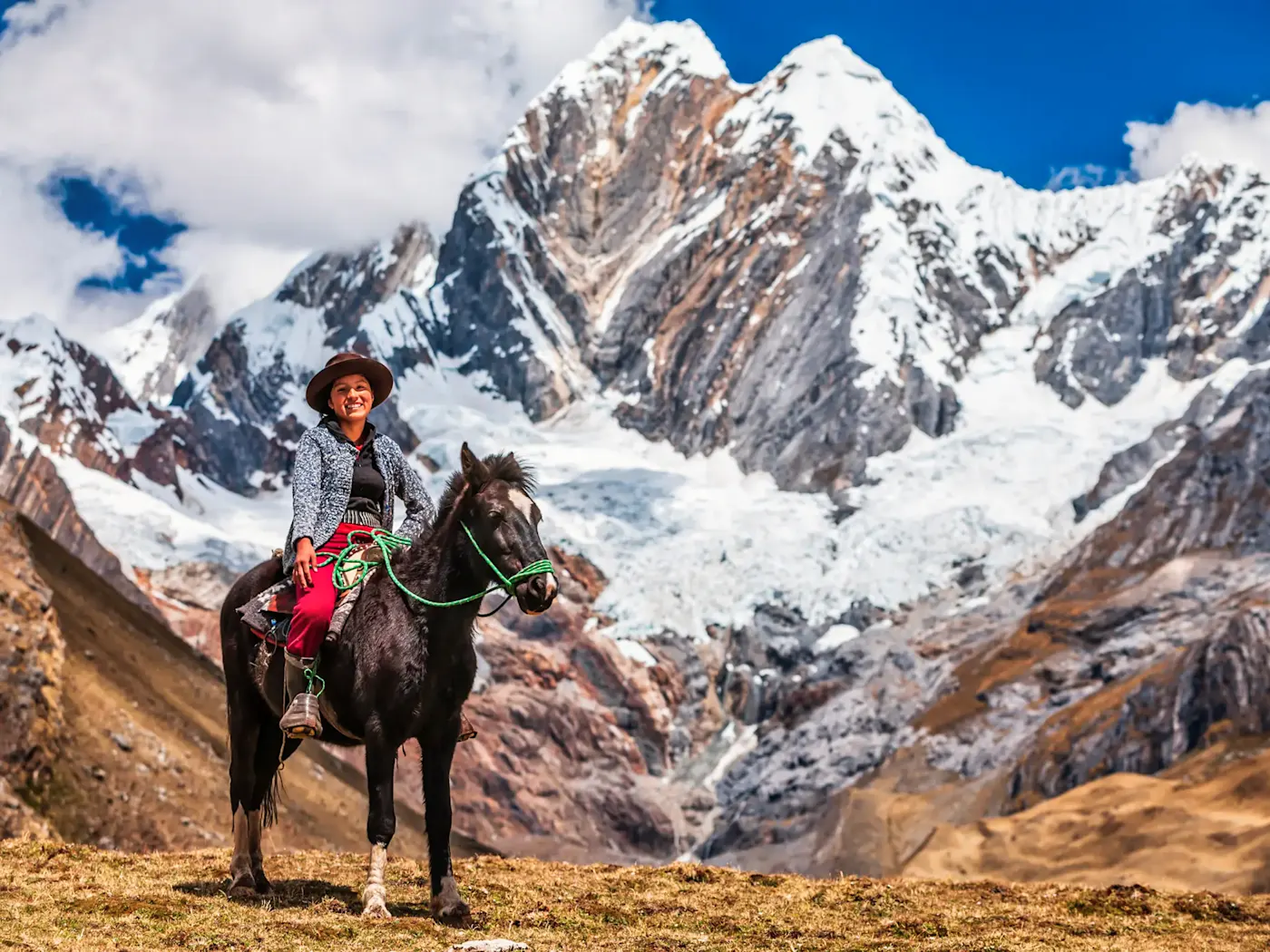 Peru, Cusco, Anden, Pferd Eine Einheimische reitet auf einem Pferd mit schneebedeckten Anden im Hintergrund, Cusco, Peru.