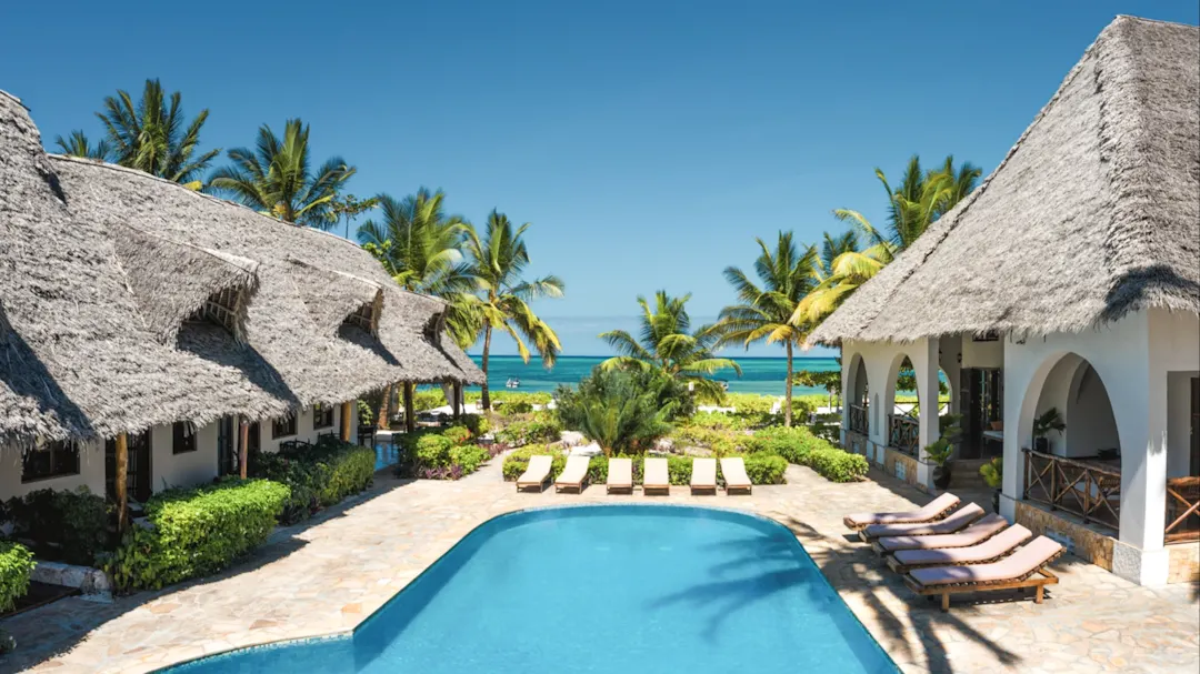 Pool mit Palmen und Strohdächern in Strandnähe. Zanzibar City, Unguja, Tansania.