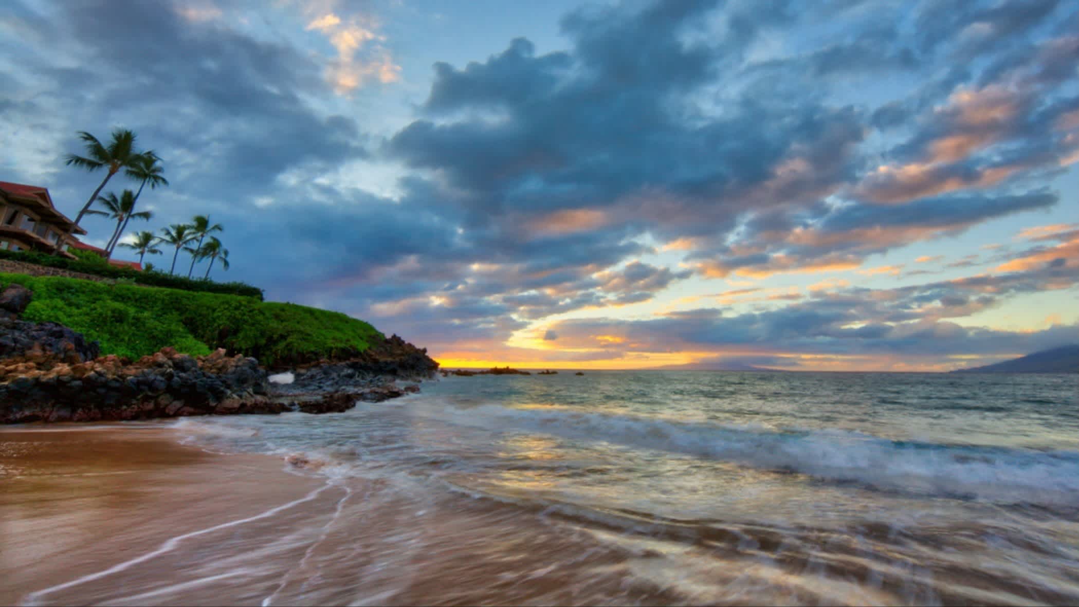 Der Wailea Beach, Maui, Hawaii, USA bei Sonnendämmerung und mit Blick auf das Meer und Palmen sowie einer Villa am Strand.