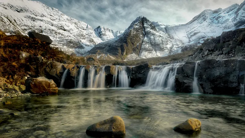 Waterfall with snow-capped mountains and green valley. Fairy Pools, Isle of Skye, Scotland.