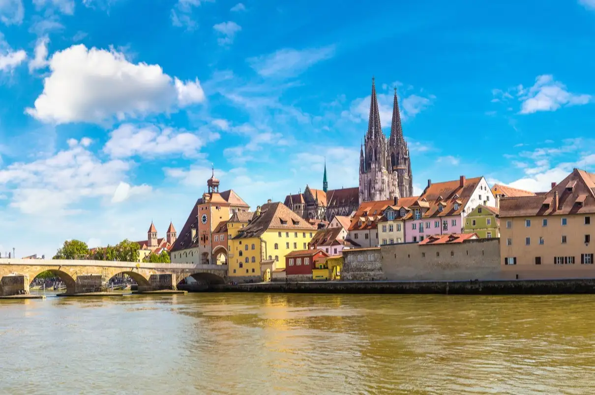 Deutschland, Regensburg, Dom Stadtansicht von Regensburg mit Dom, bunten Häusern und Steinbrücke über die Donau unter blauem Himmel mit weißen Wolken.