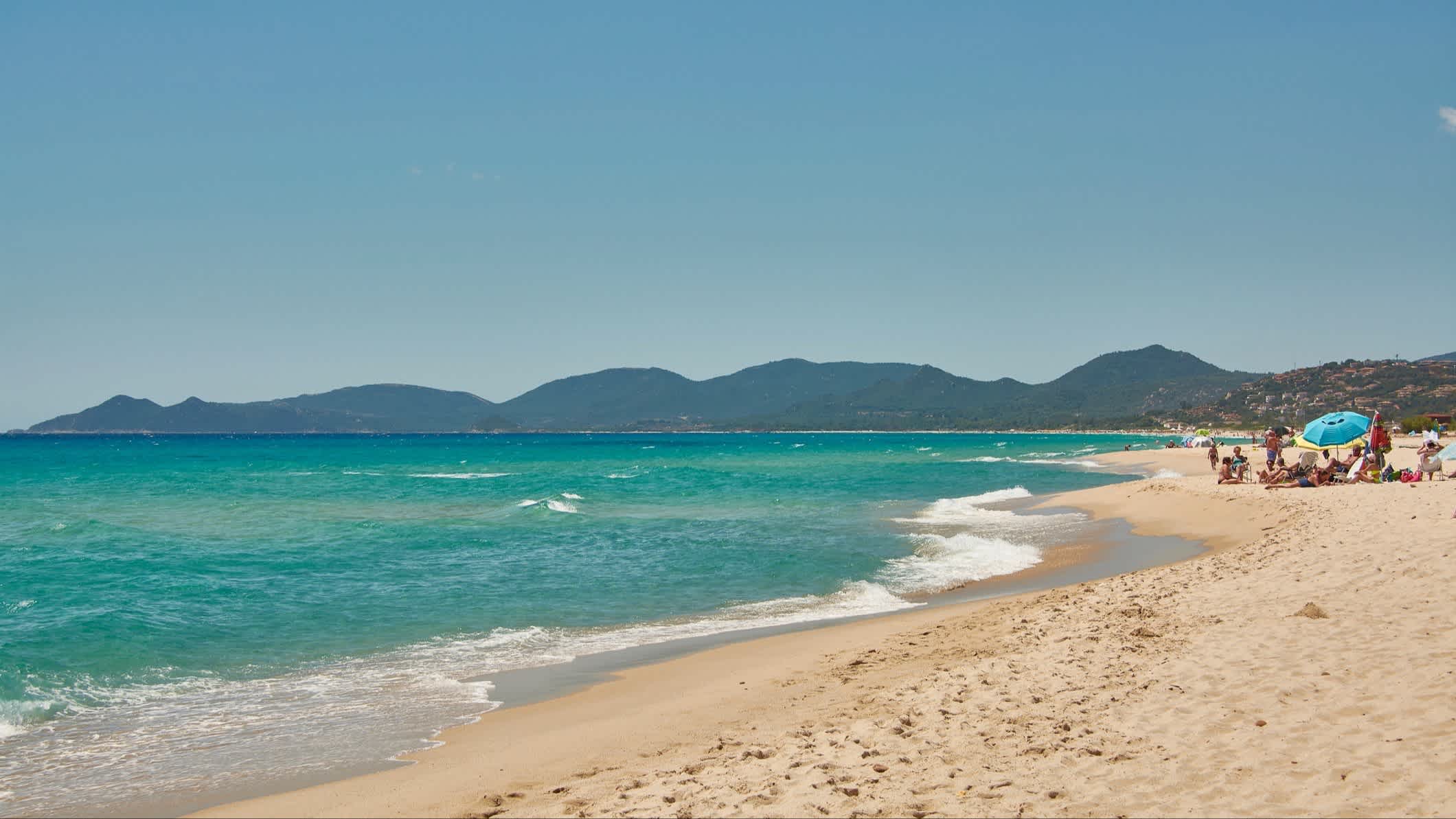 Die Landschaft des Strandes von Costa Rei in Muravera, Sardinien, Italien bei sonnigem Wetter und mit Menschen am Strand.