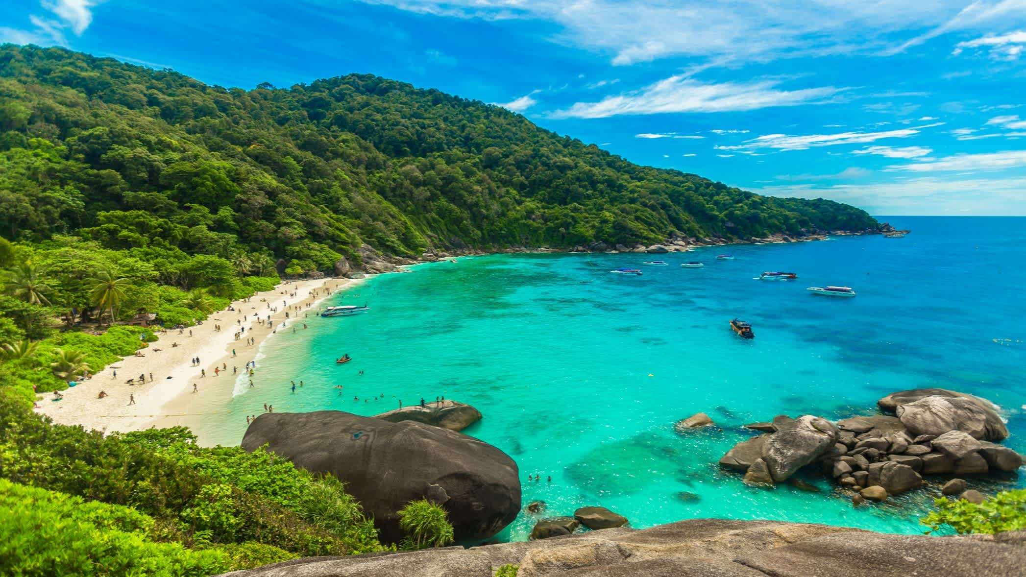 Blick auf eine Bucht auf Phuket, Thailand, mit türkisblauem Wasser, Sandstrand und saftiggrünen Hügeln.