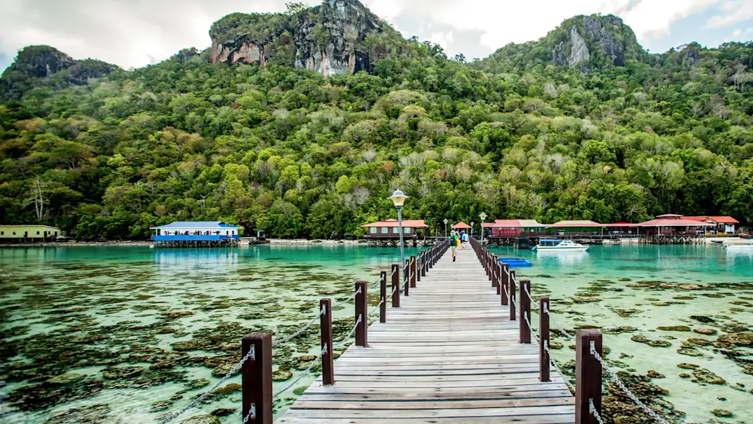 Holzsteg mit Blick auf grüne Hügel und Meer. Semporna, Sabah, Malaysia.