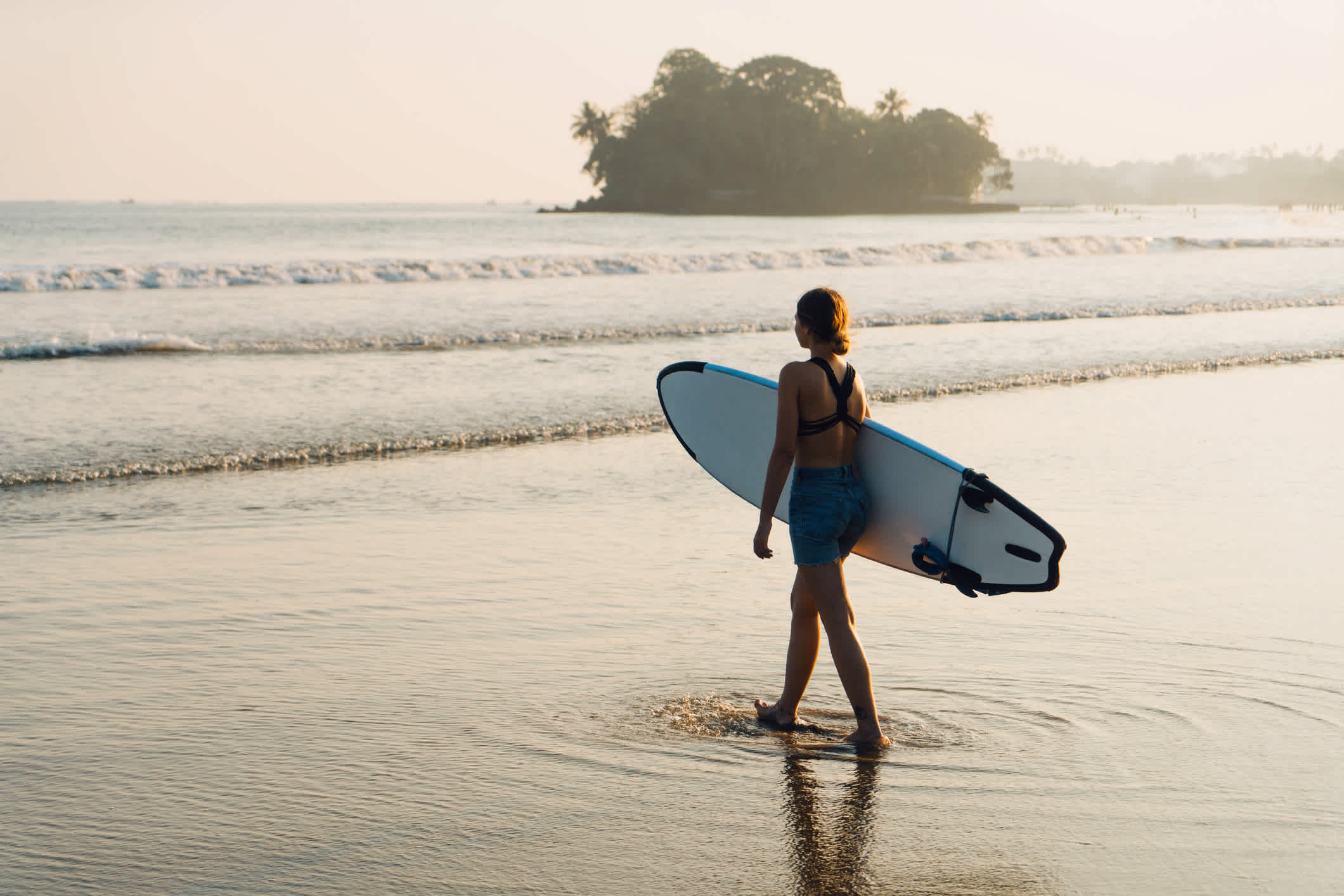 Junge Frau steht mit Surfbrett am Strand, Weligama