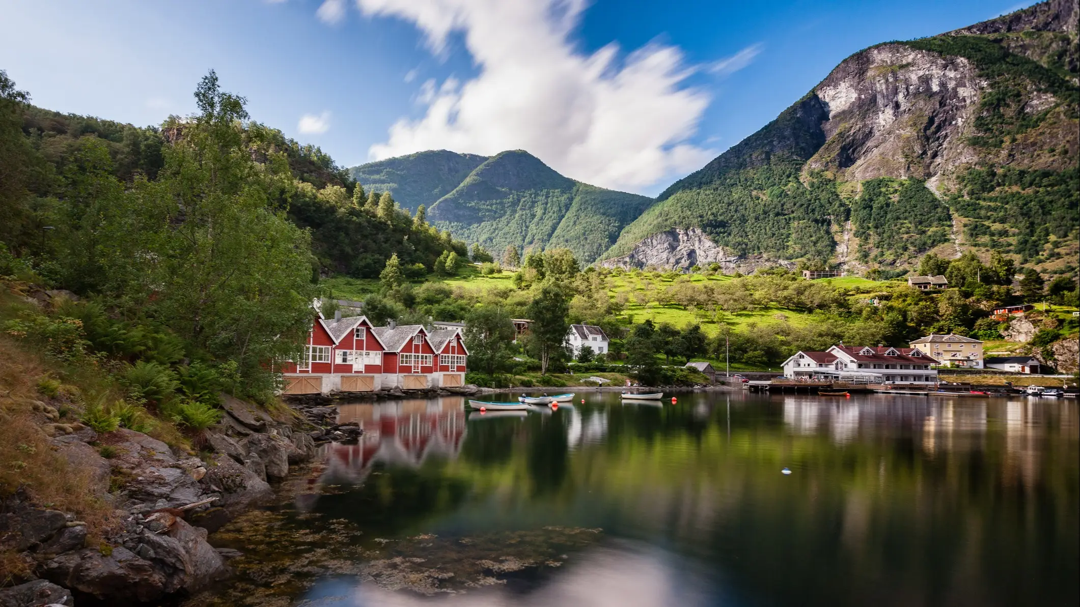 Maisons en bois rouge sur les rives d'un fjord tranquille entouré de montagnes et de forêts verdoyantes, Sognefjord, Norvège,