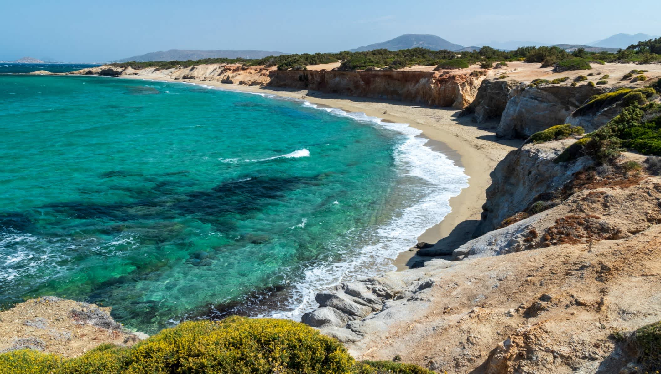 Blick auf den Sandstrand Paralia Hawaii in Naxos, Griechenland, umgeben von Felsen und türkisblauem Wasser.