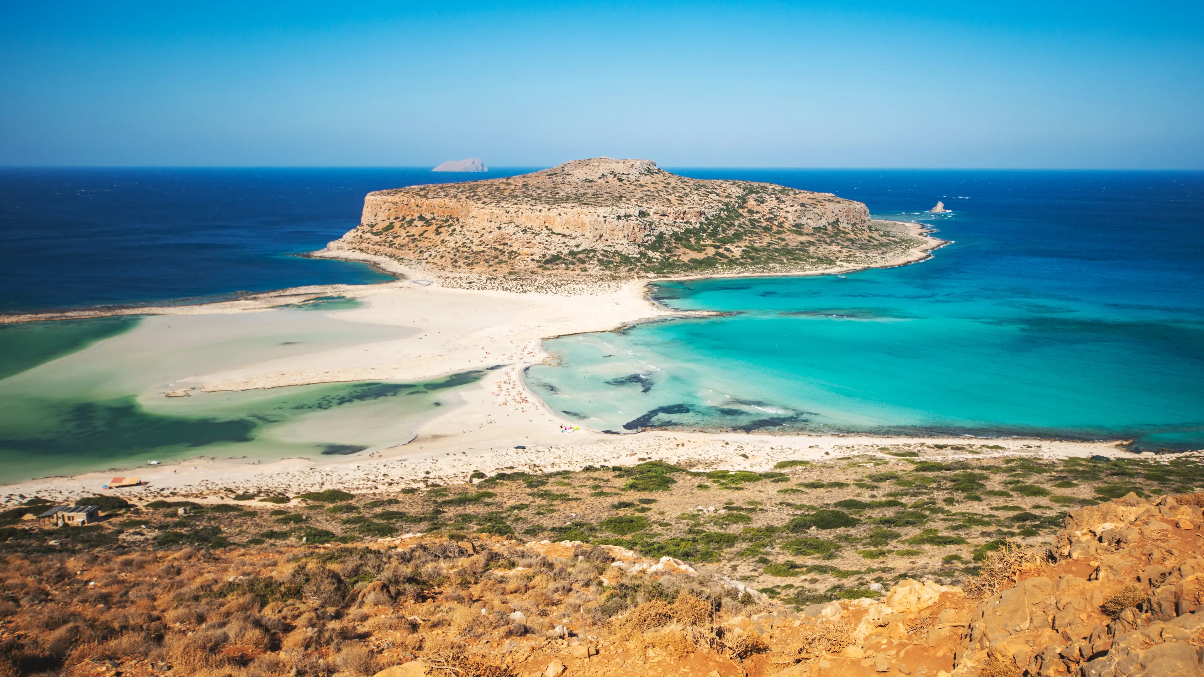 Lagune et langue de sable en Crète, entourées d'un paysage aride.