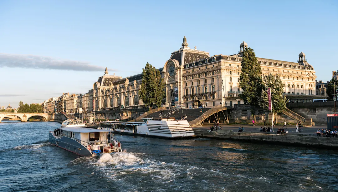 Musée d'Orsay in Paris mit Ausflugsboot auf der Seine bei Sonnenuntergang, historisches Gebäude mit großer Uhr.
