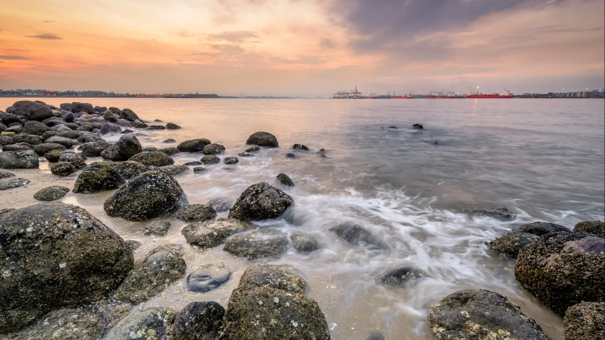 Coucher de soleil sur la plage Punggol avec des rochers au premier plan, Singapour.