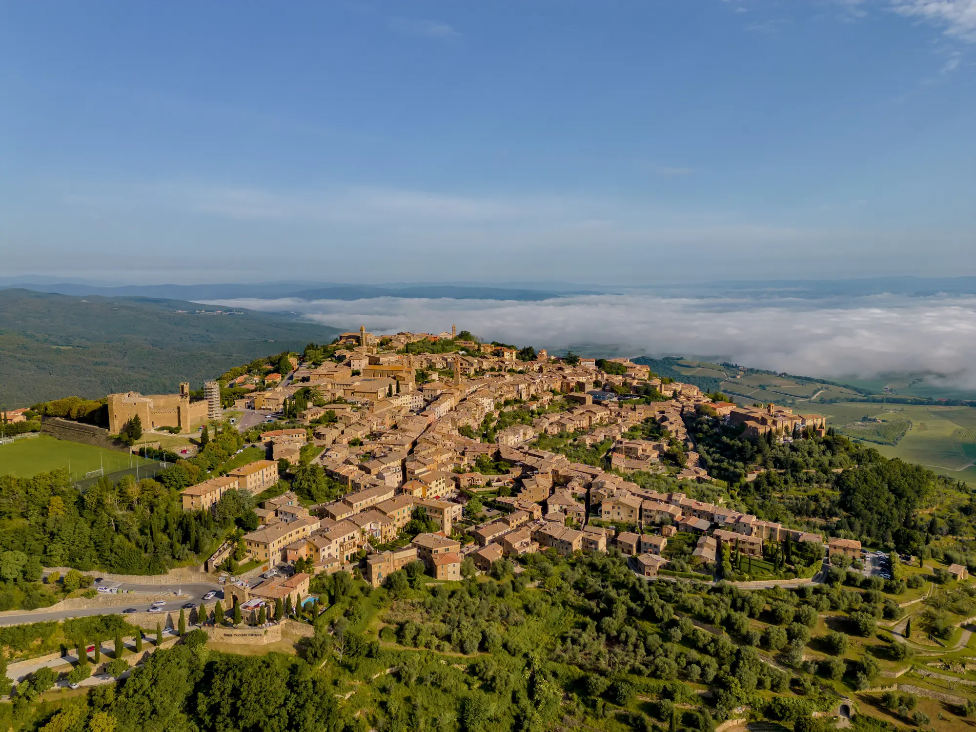 Luftaufnahme des Bergdorfes Montalcino inmitten einer grünen Hügellandschaft