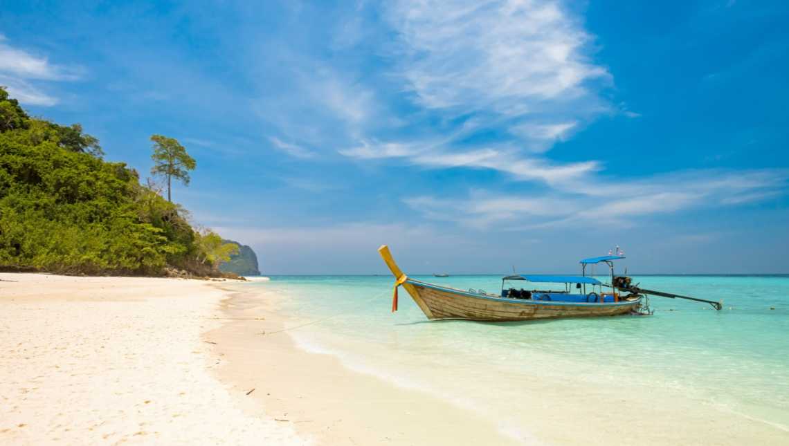 Ein Boot ankert auf einem wunderschönen Strand mit kristallklarem Meer und weißem Sand 