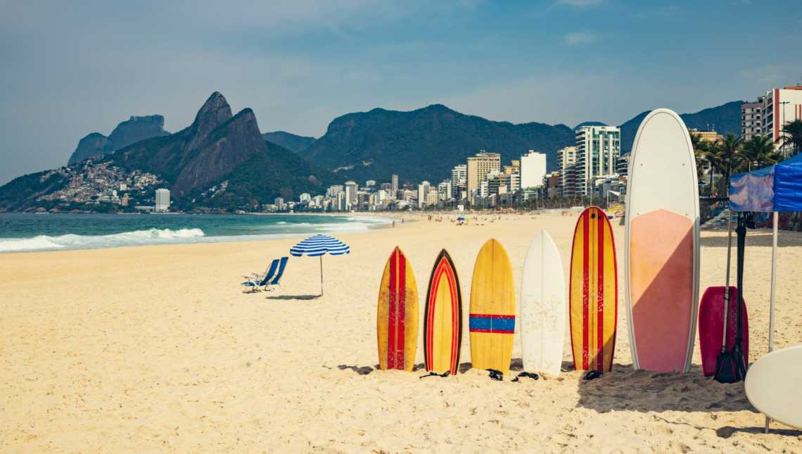 Plage d'Ipanema avec planches de surf et parasol sur le sable en premier plan, Rio de Janerio, Brésil.