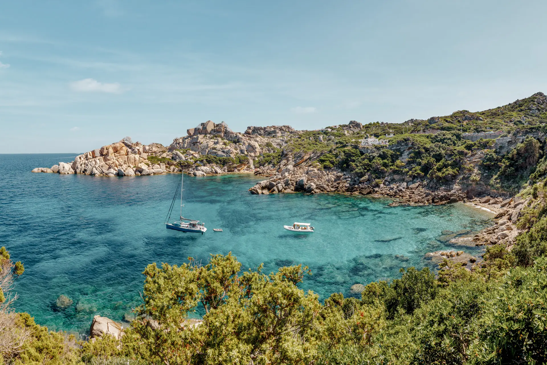 Klare, türkisfarbene Bucht mit Felsen und grünem Ufer bei Sardinien, Italien.