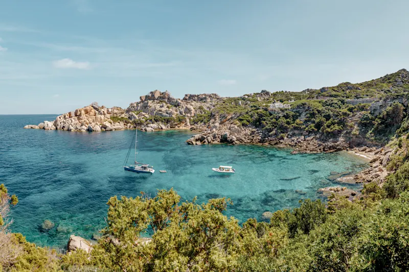 Clear, turquoise bay with rocks and a green shore near Sardinia, Italy.