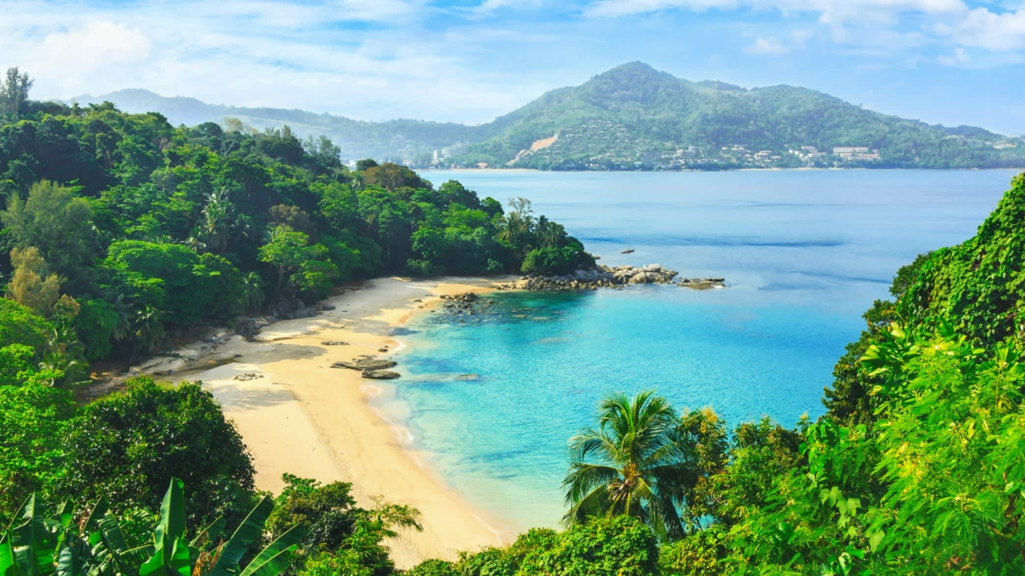 Vue sur la baie de Laem Singh Beach avec des collines d'un vert luxuriant, une plage de sable doré, une mer turquoise et un paysage montagneux en arrière-plan, à Phuket en Thaïlande.