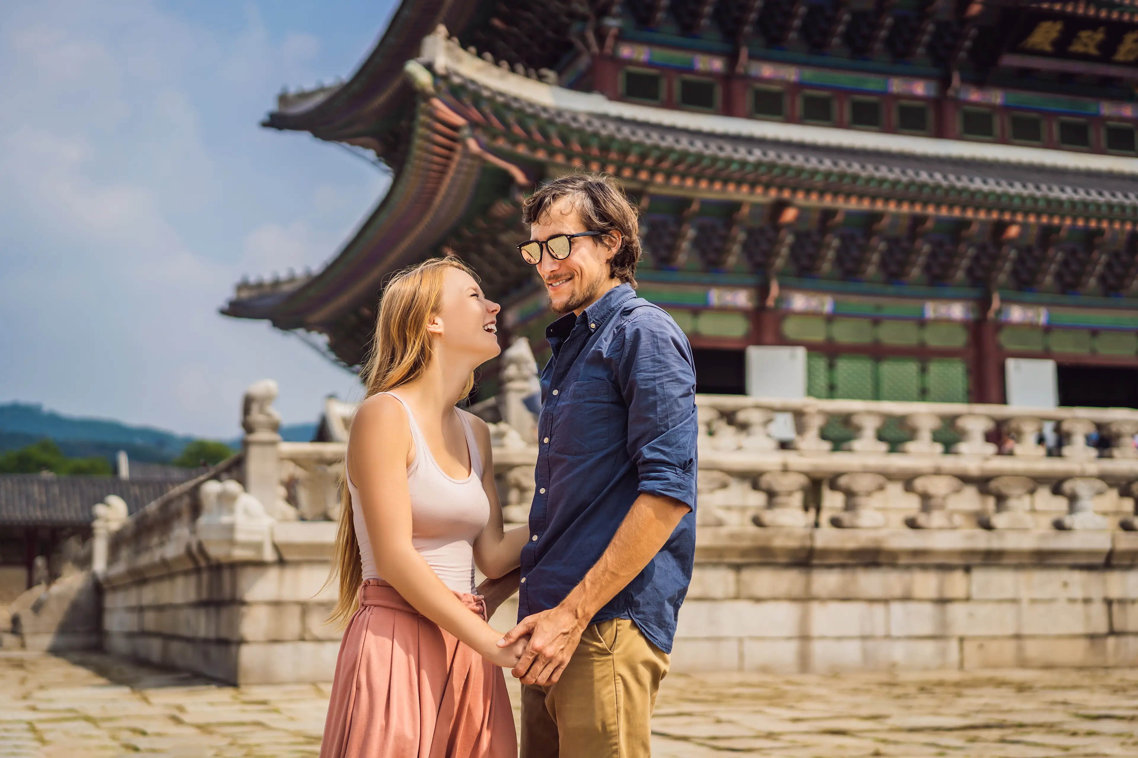 Südkorea, Flitterwochen Paar hält sich an den Händen und lächelt sich an; im Hintergrund ein Tempel.