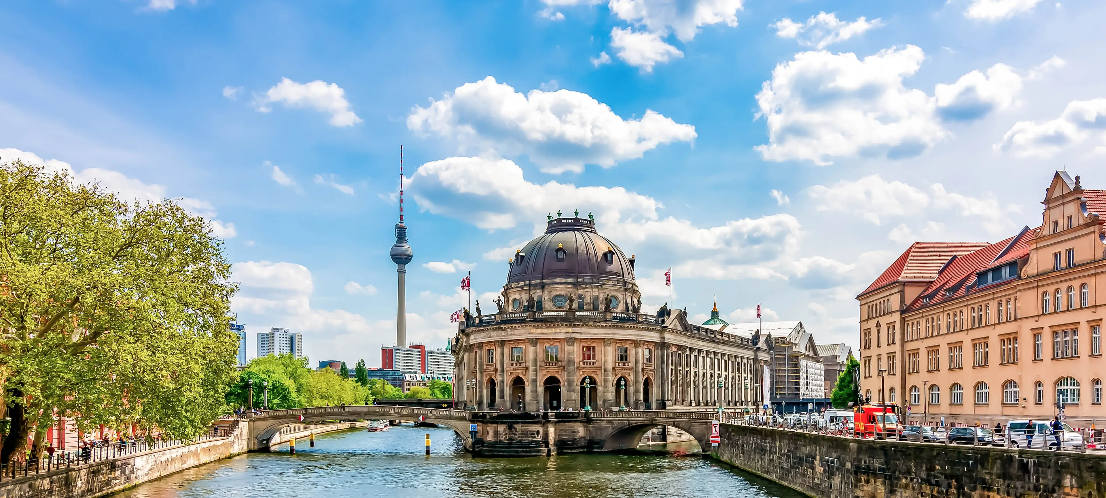 Bodemuseum auf der Museumsinsel in Berlin mit Fernsehturm im Hintergrund, umgeben von der Spree bei blauem Himmel.