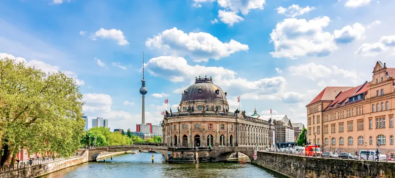 Bodemuseum auf der Museumsinsel in Berlin mit Fernsehturm im Hintergrund, umgeben von der Spree bei blauem Himmel.