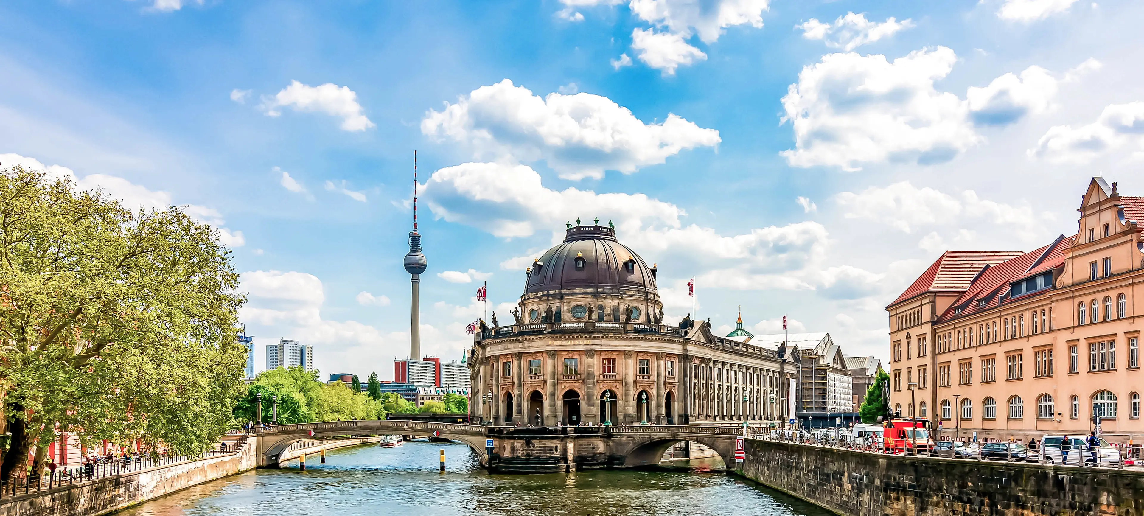 Bodemuseum auf der Museumsinsel in Berlin mit Fernsehturm im Hintergrund, umgeben von der Spree bei blauem Himmel.