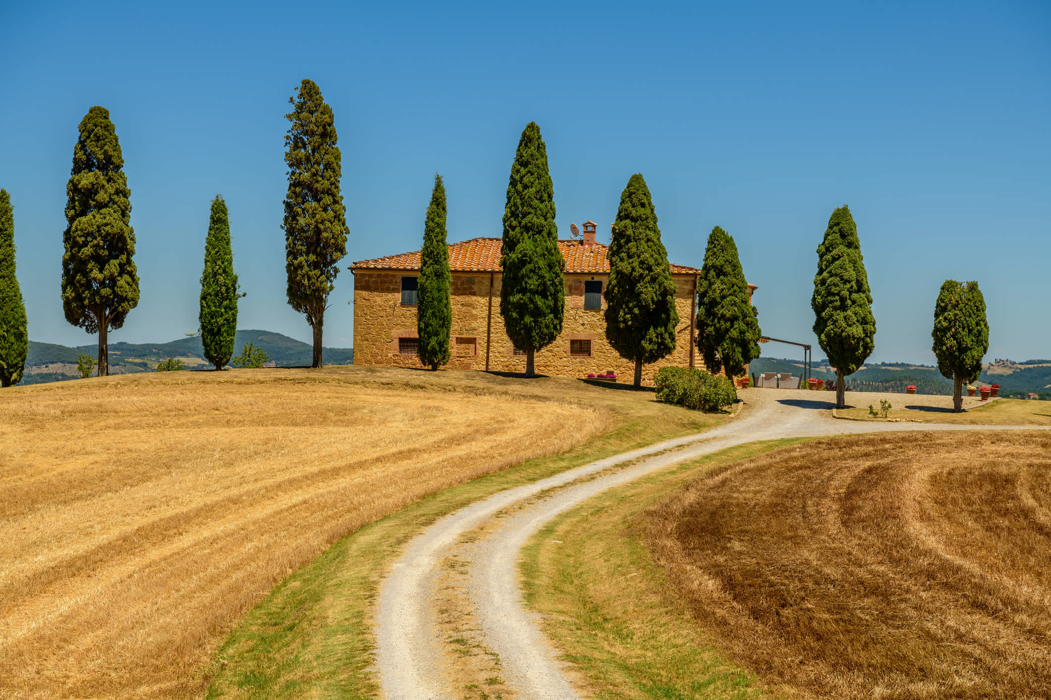 Vue sur un chemin de terre avec des cyprès et une ferme en Toscane