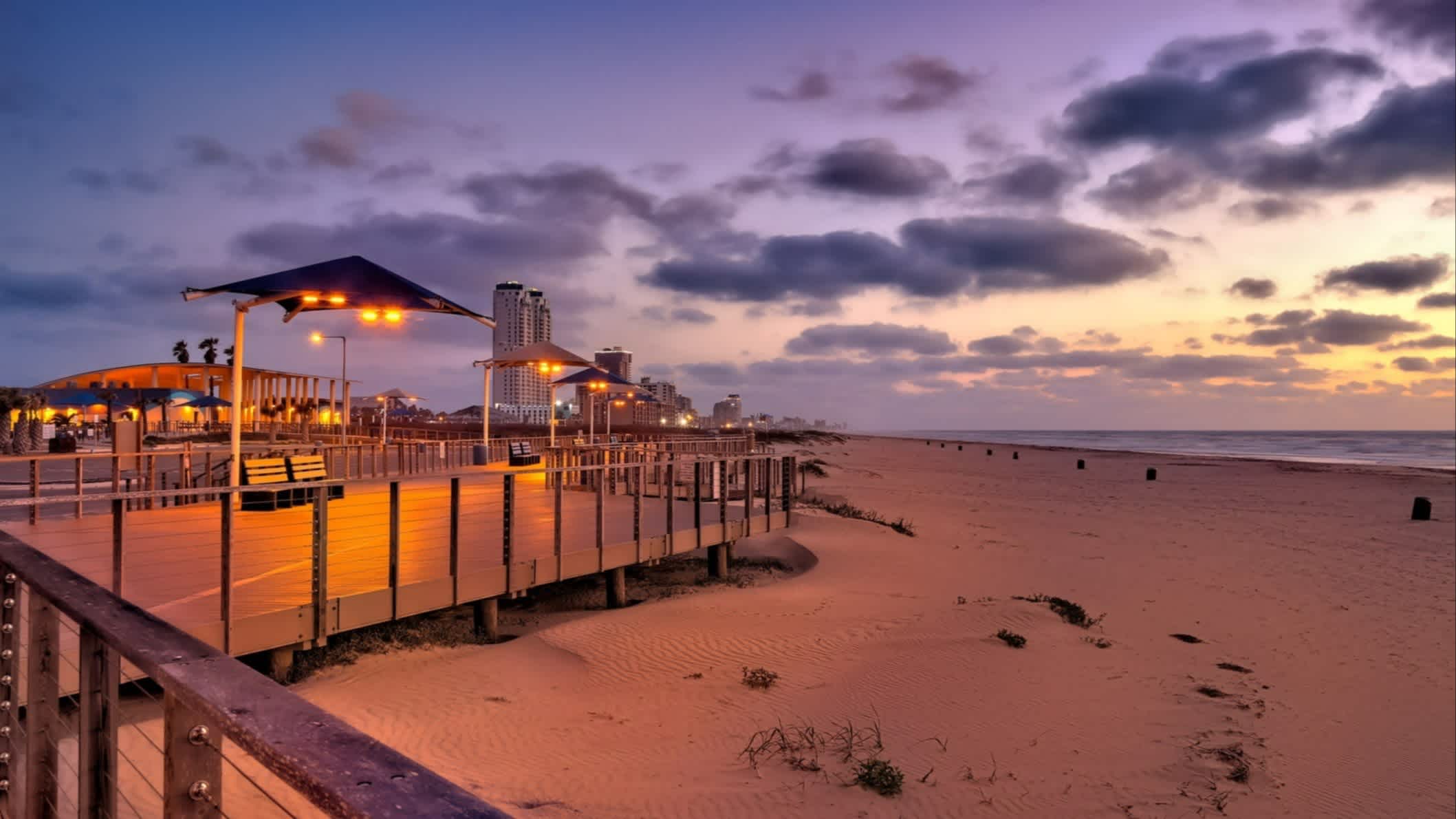 Der Strand Isla Blanca Beach, South Padre Island, Texas, USA bei Abenddämmerung mit Blick auf die beleuchtete Promenade.