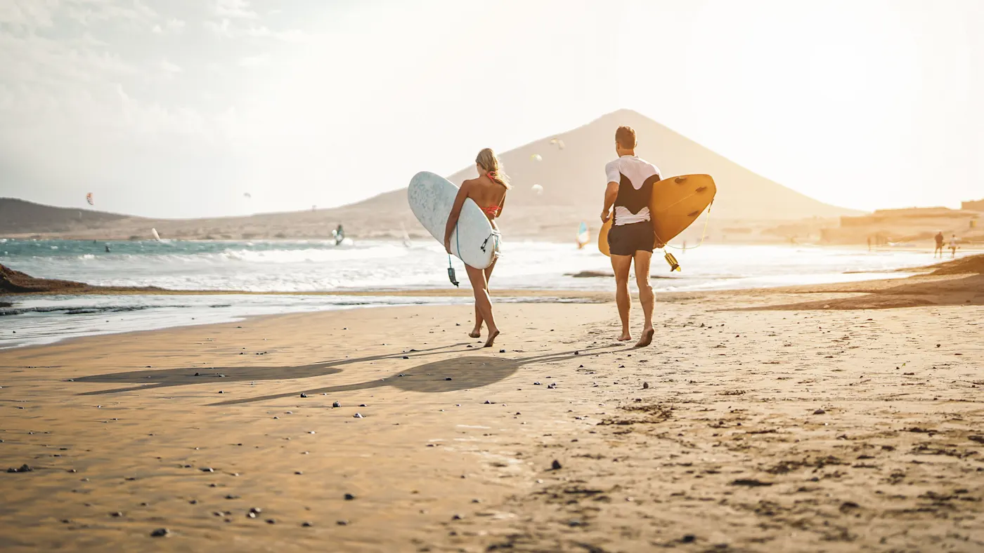 États-Unis, Californie, Plage Couple de surfeurs marchant sur la plage au coucher du soleil, Californie, États-Unis.