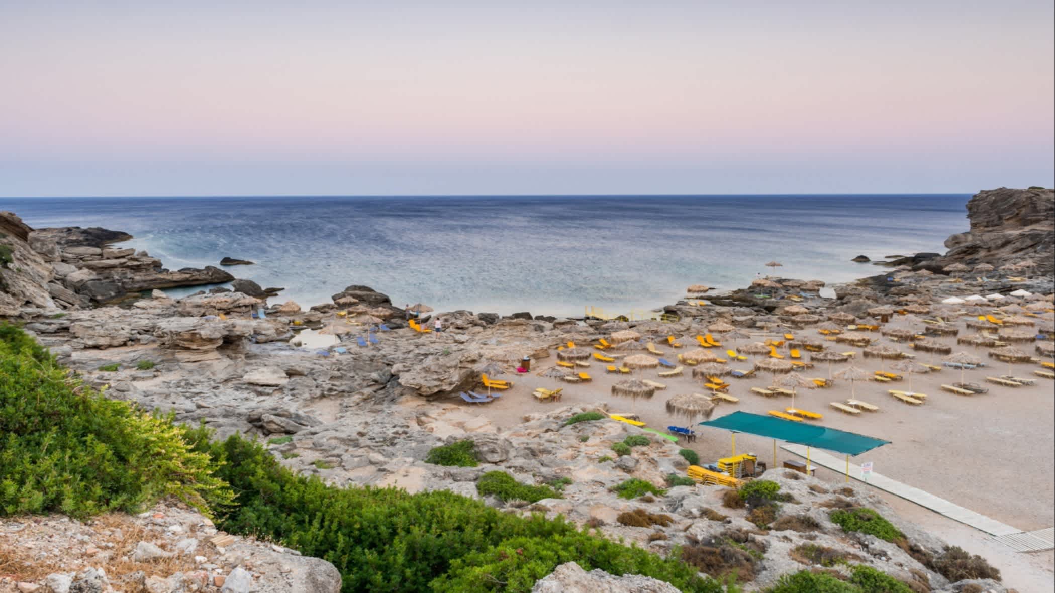 Der Strand in Kallithea in einer Bucht gelegen mit Schirmen und Liegen bei Sonnendämmerung, Rhodes, Griechenland.