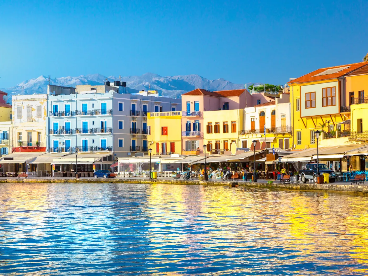 Griechenland Kreta Bunte Häuserzeile am Hafen von Chania auf Kreta mit blauem Wasser im Vordergrund und Bergen im Hintergrund.
