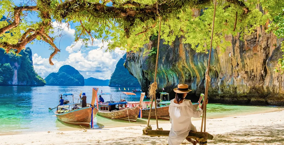 Frau auf Schaukel am Strand, Longtail-Boote im Wasser. Krabi, Südthailand, Thailand.
