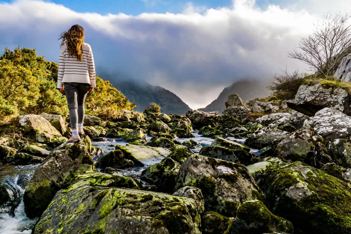 Eine Wanderin auf Steinen am Fluss in Gap of Dunloe, County Kerry, Irland.