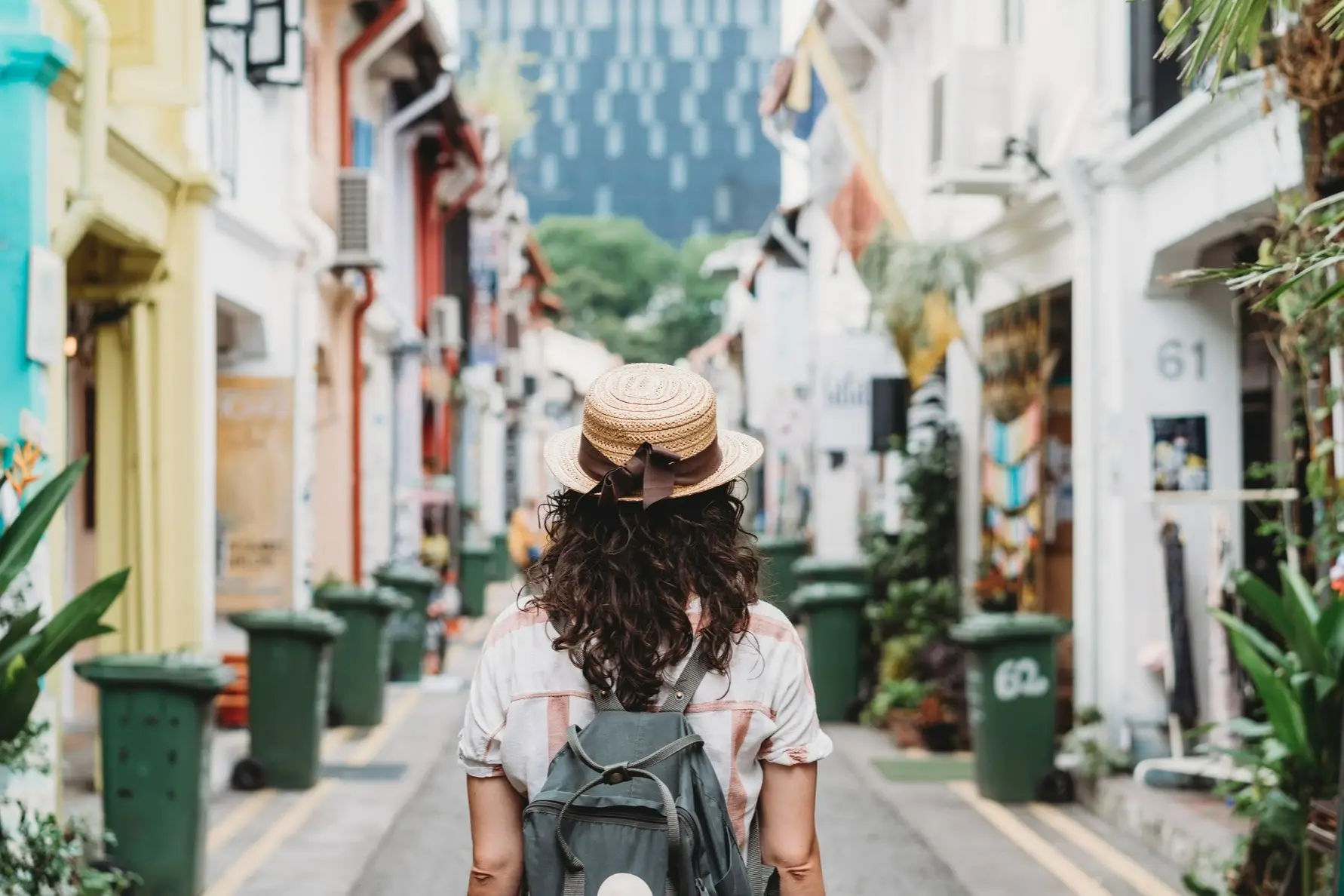 Touriste de dos avec sac à dos et chapeau de soleil dans une rue calme aux façades colorées à Singapour