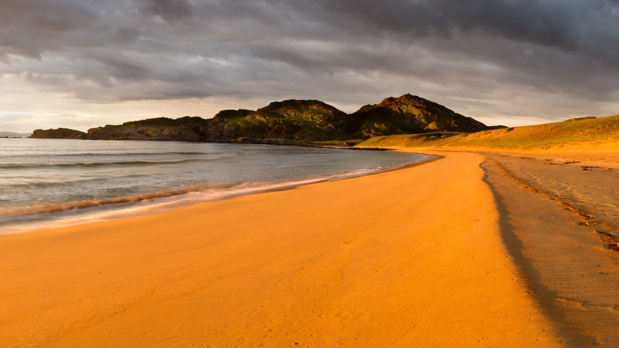 Lumière dorée sur le sable de la baie de Kiloran à Colonsay, Écosse par temps nuageux