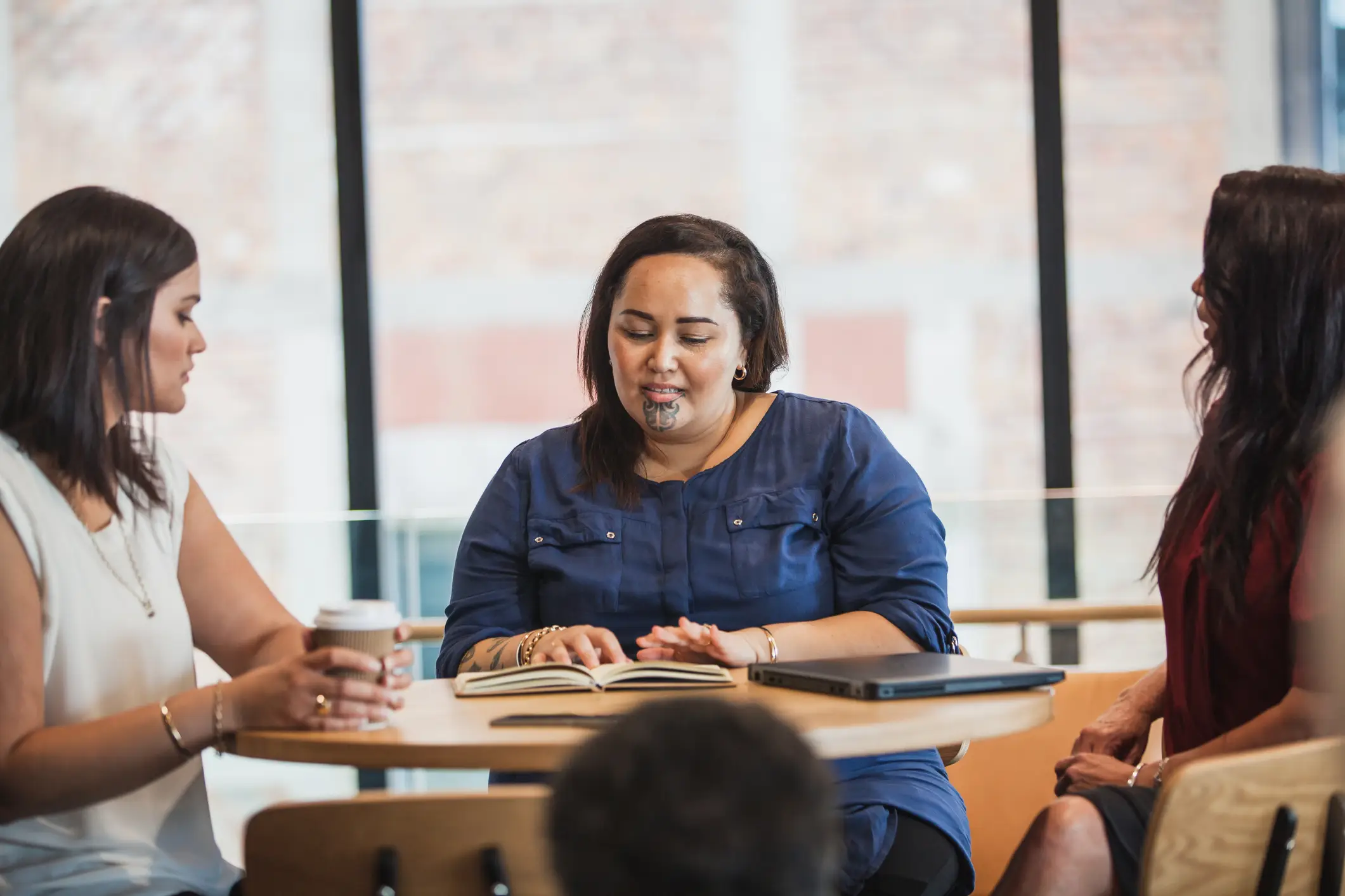 Femme maori avec les tatouages traditionnelles avec un livre assise à une table