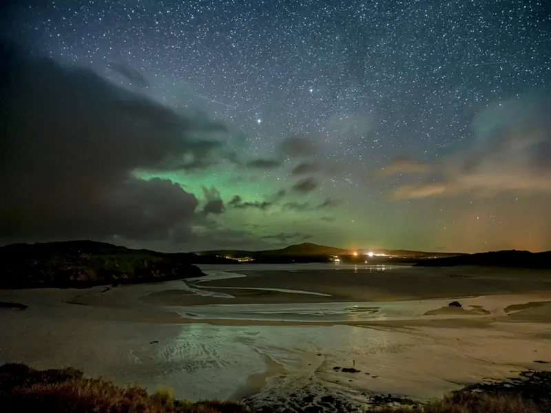 Northern lights over sandy bay and starry sky. Lerwick, Shetland, Scotland.