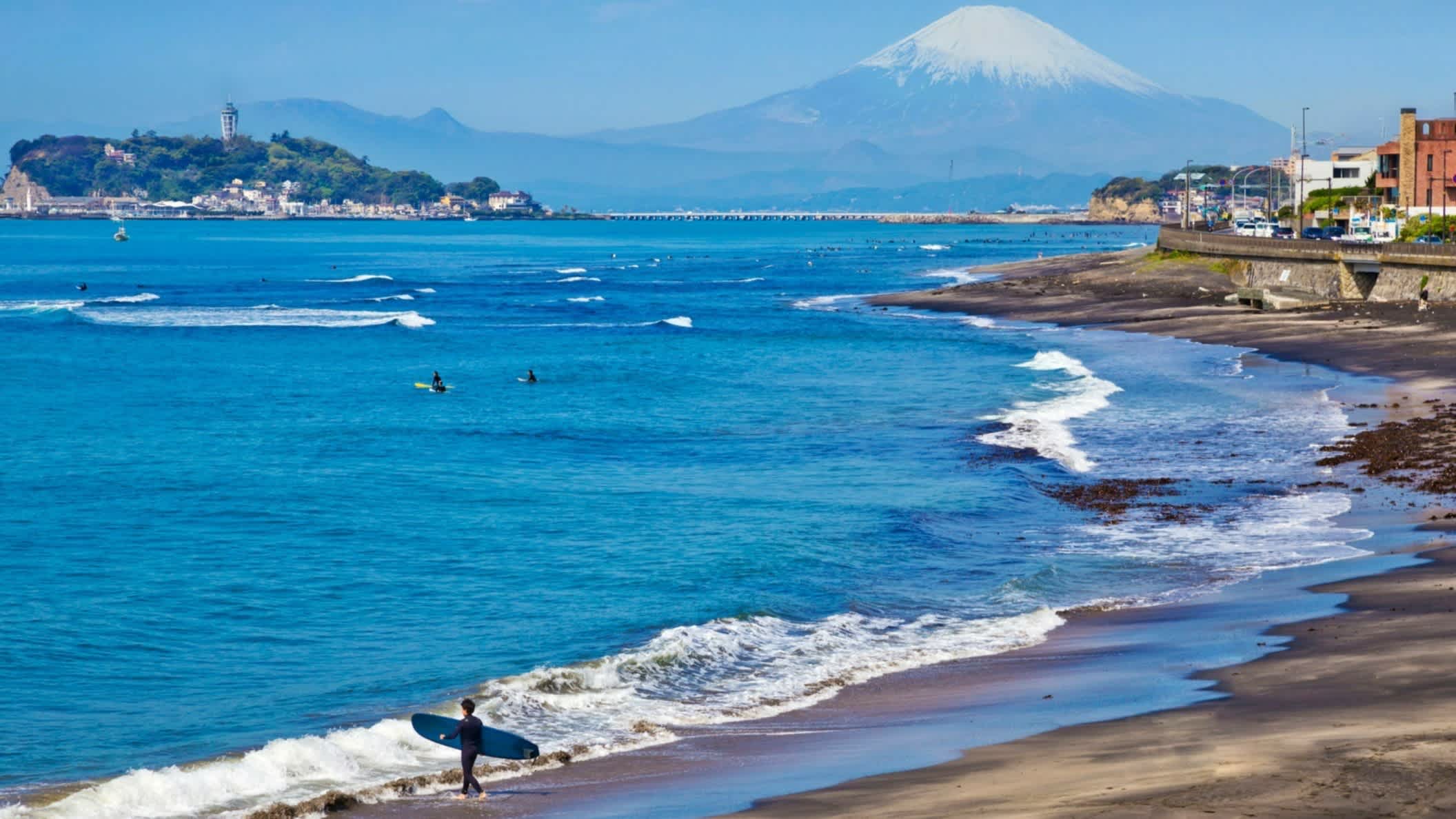 Surfer am Naturstrand von Kamakura, Kanagawa, Japan mit dem Mount Fuji im Hintergrund.